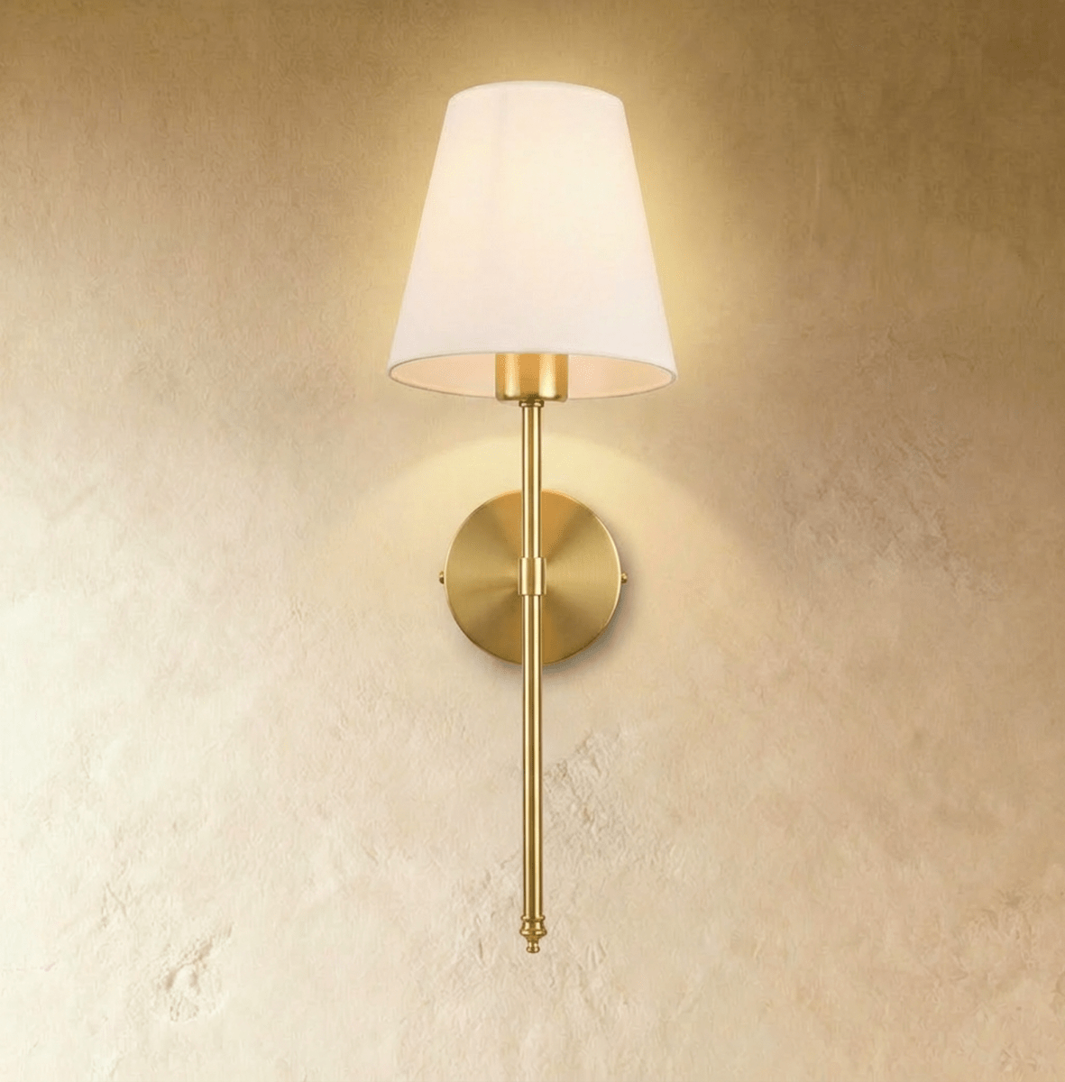 Clérachic brushed gold wall sconce with a white tapered fabric shade on a long slim rod, lit warm on a plaster wall.