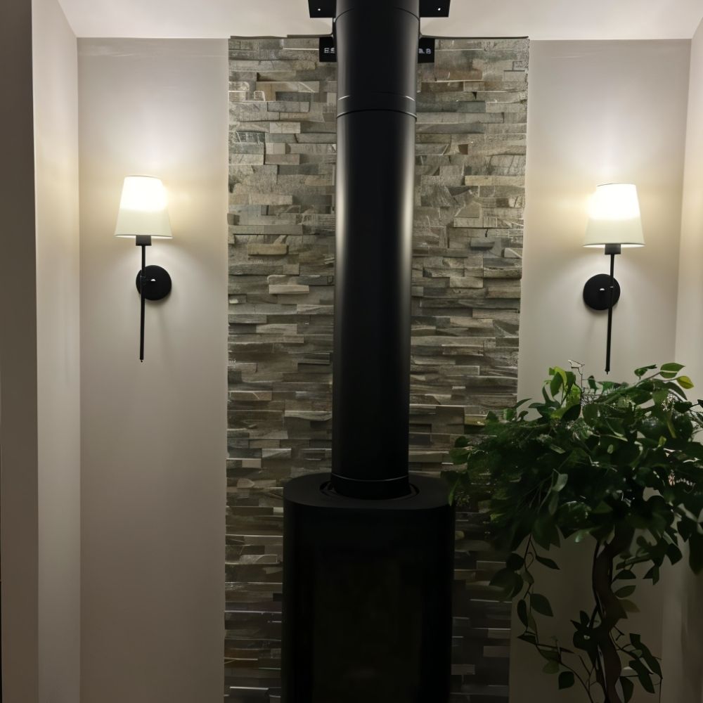 Clérachic pair of black wall sconces with white fabric shades either side of a stone-clad wall and a black stove flue.