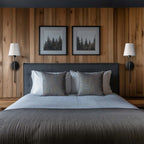Clérachic pair of black wall sconces with white shades either side of two framed prints on a timber-panelled bedroom wall.