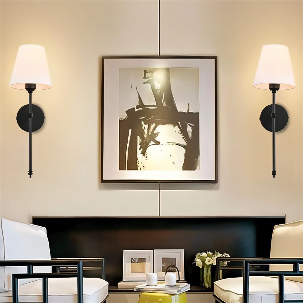 Clérachic pair of black wall sconces with white tapered shades flanking a large framed abstract print above a console.