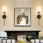Clérachic pair of black wall sconces with white tapered shades flanking a large framed abstract print above a console.