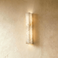 Clérachic slim alabaster bar wall light, lit, glowing up and down a limewashed wall in warm cream tones