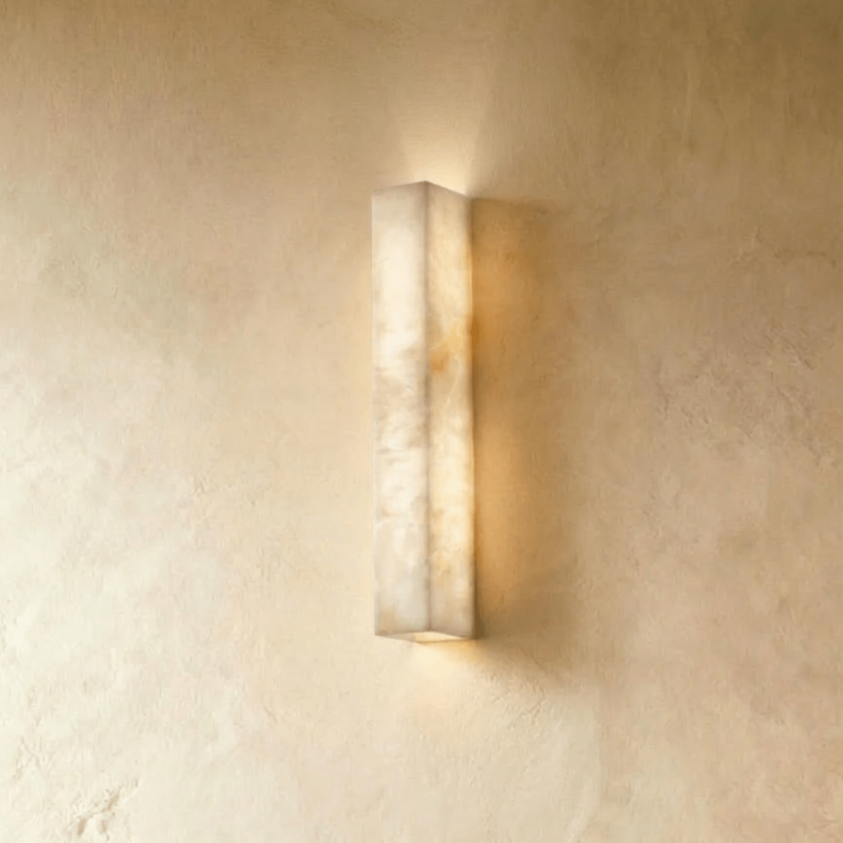 Clérachic slim alabaster bar wall light, lit, glowing up and down a limewashed wall in warm cream tones