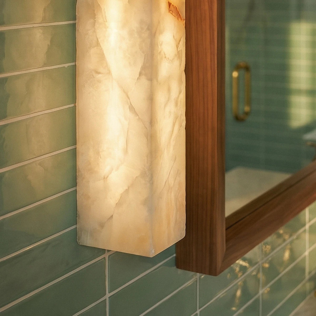 Close view of the Clérachic alabaster bar wall light glowing beside a walnut mirror frame on glossy green tiles