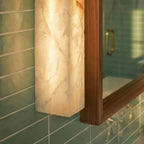 Close view of the Clérachic alabaster bar wall light glowing beside a walnut mirror frame on glossy green tiles