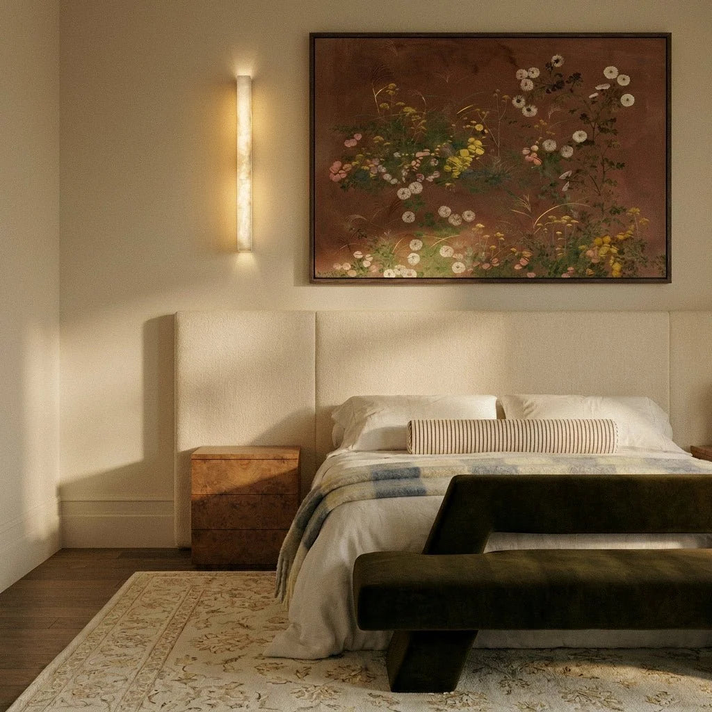 Clérachic long alabaster bar wall light beside a floral painting above an upholstered bed in a warm cream bedroom