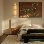 Clérachic long alabaster bar wall light beside a floral painting above an upholstered bed in a warm cream bedroom