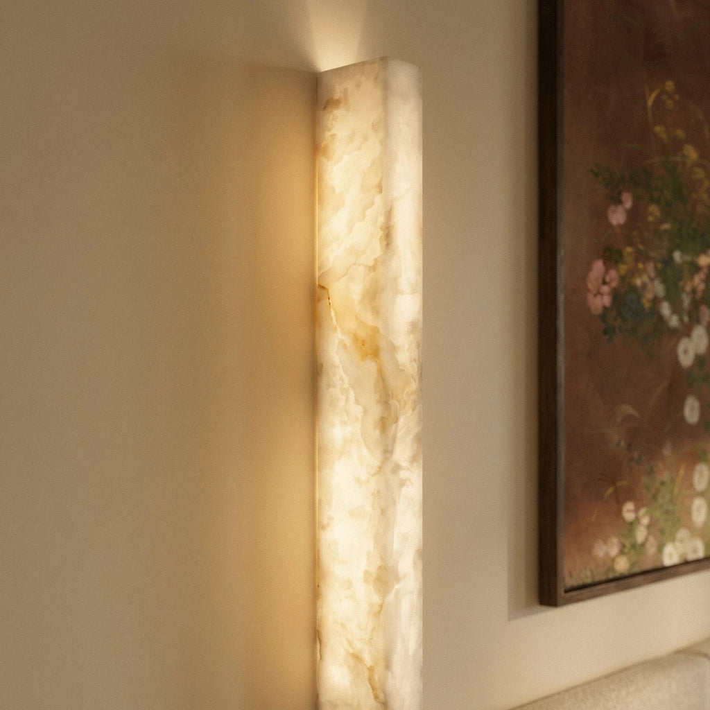 Detail of the Clérachic alabaster bar wall light, its lit stone showing amber and cream veining beside a framed painting