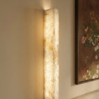 Detail of the Clérachic alabaster bar wall light, its lit stone showing amber and cream veining beside a framed painting