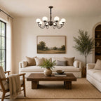A Clérachic chandelier with eight white globes hangs over a cream sofa, a rustic coffee table and a landscape painting in a calm sitting room.