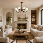 A Clérachic globe chandelier hung in a living room with a stone fireplace, built-in shelves and two cream sofas on a jute rug.