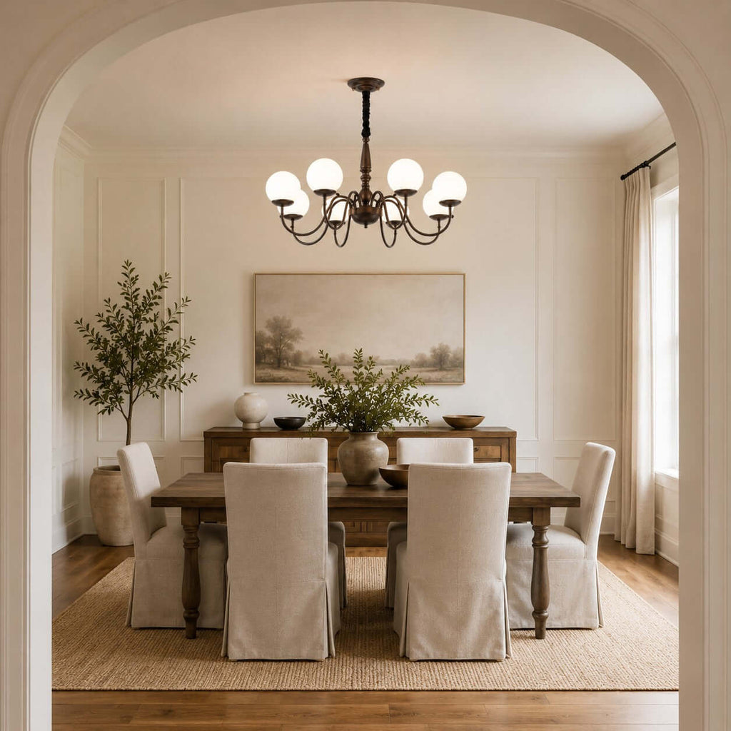 Looking through an arched doorway, a Clérachic chandelier with white globes hangs above a dining table with slip-covered chairs.