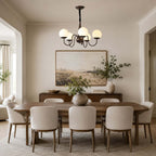A Clérachic chandelier hung above a long walnut dining table with cream chairs and a large framed landscape on the wall.