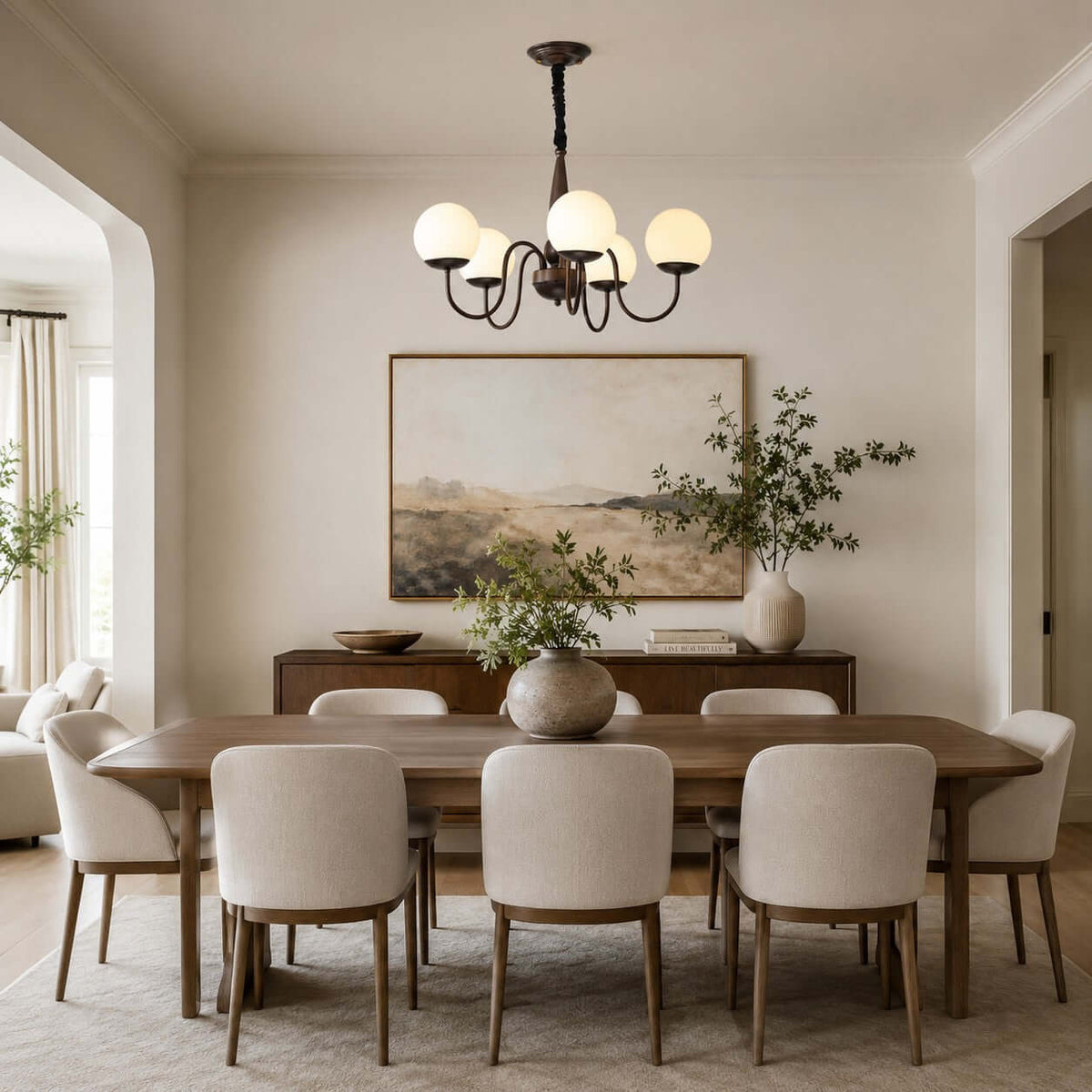 A Clérachic chandelier hung above a long walnut dining table with cream chairs and a large framed landscape on the wall.