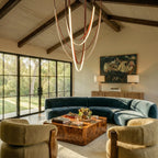 Clérachic leather chandelier hung beneath vaulted beams, its glowing loops suspended above a curved blue sofa.