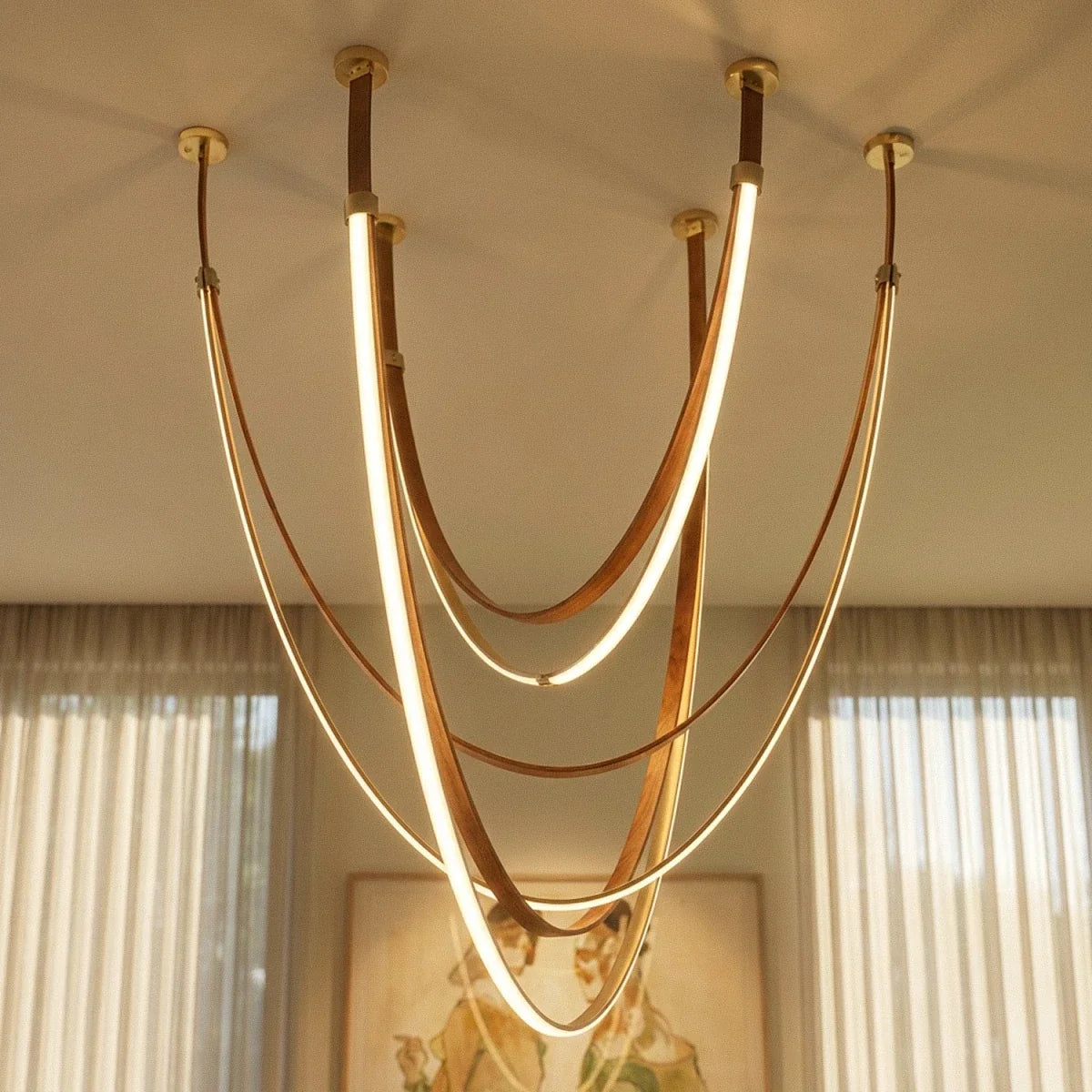 Close-up of the Clérachic leather chandelier's brass ceiling mounts and glowing leather loops against sheer curtains.