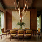 Clérachic leather chandelier hung over a long dining table, its glowing loops set against a sketch-style artwork.