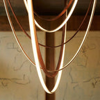 Close-up of the Clérachic leather chandelier's nested leather loops glowing warm white against a charcoal sketch.