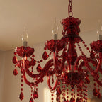 Detail of a Clérachic red crystal chandelier with candle bulbs, ribbed floral cups, curved arms and beaded drops in warm light.