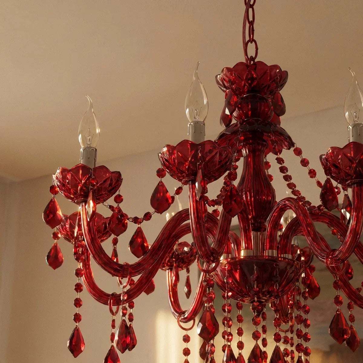 Detail of a Clérachic red crystal chandelier with candle bulbs, ribbed floral cups, curved arms and beaded drops in warm light.