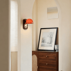 Small in a wider view, this Clérachic wall light is lit beside an arched doorway, with a framed print above a walnut and rattan cabinet.