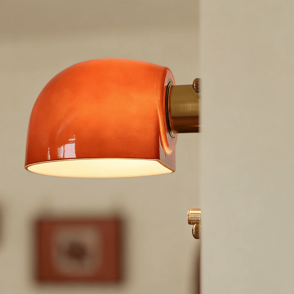 Close view of the glossy lit dome and brass arm on this Clérachic wall light, with a soft-focus frame and brass knob behind.