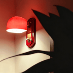 Lit dome of this Clérachic wall light glowing bright red, with the shadow of a large plant leaf falling across the wall.