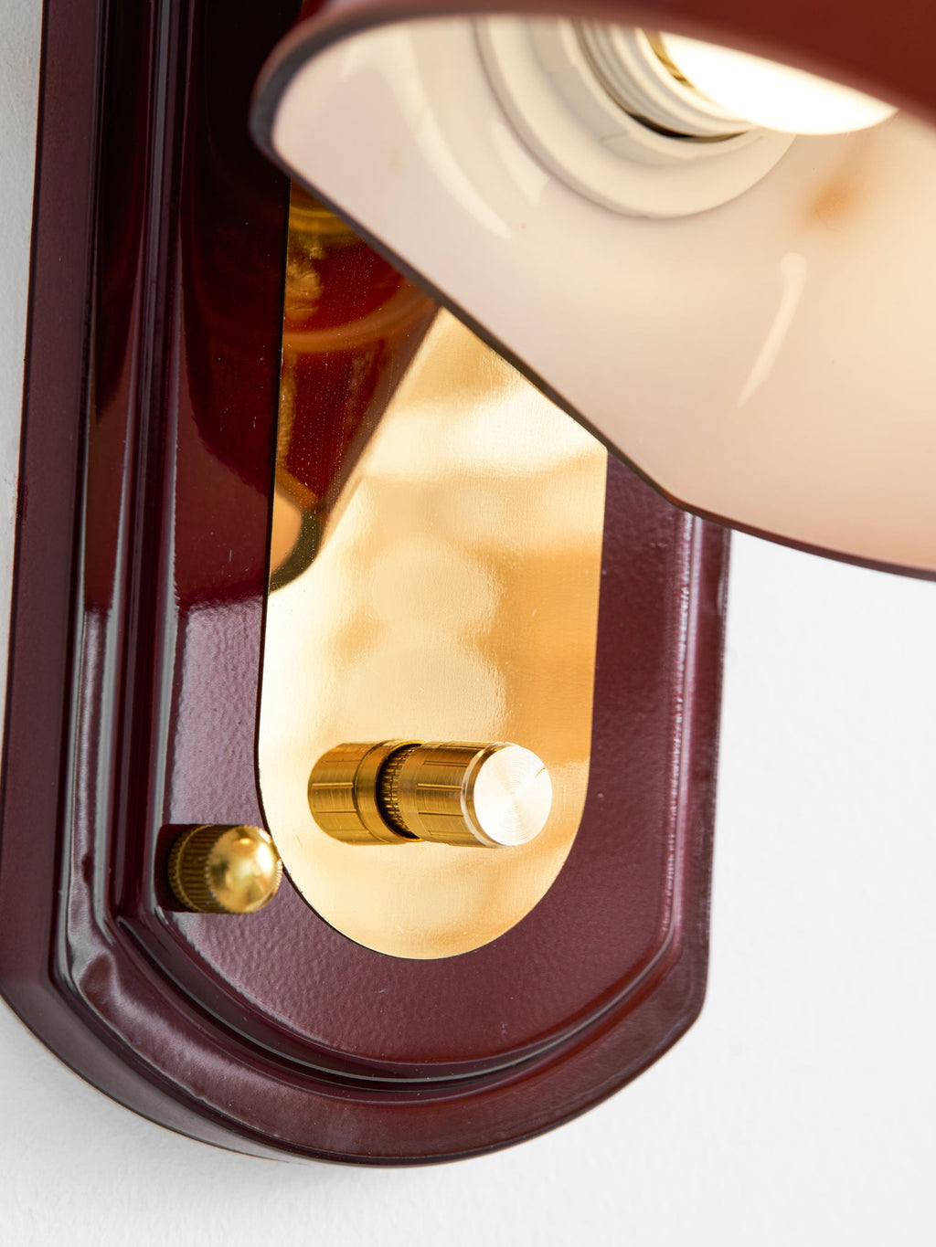 Close view of the red backplate, gold panel and brass knob on this Clérachic wall light, with the dome's inner socket above.