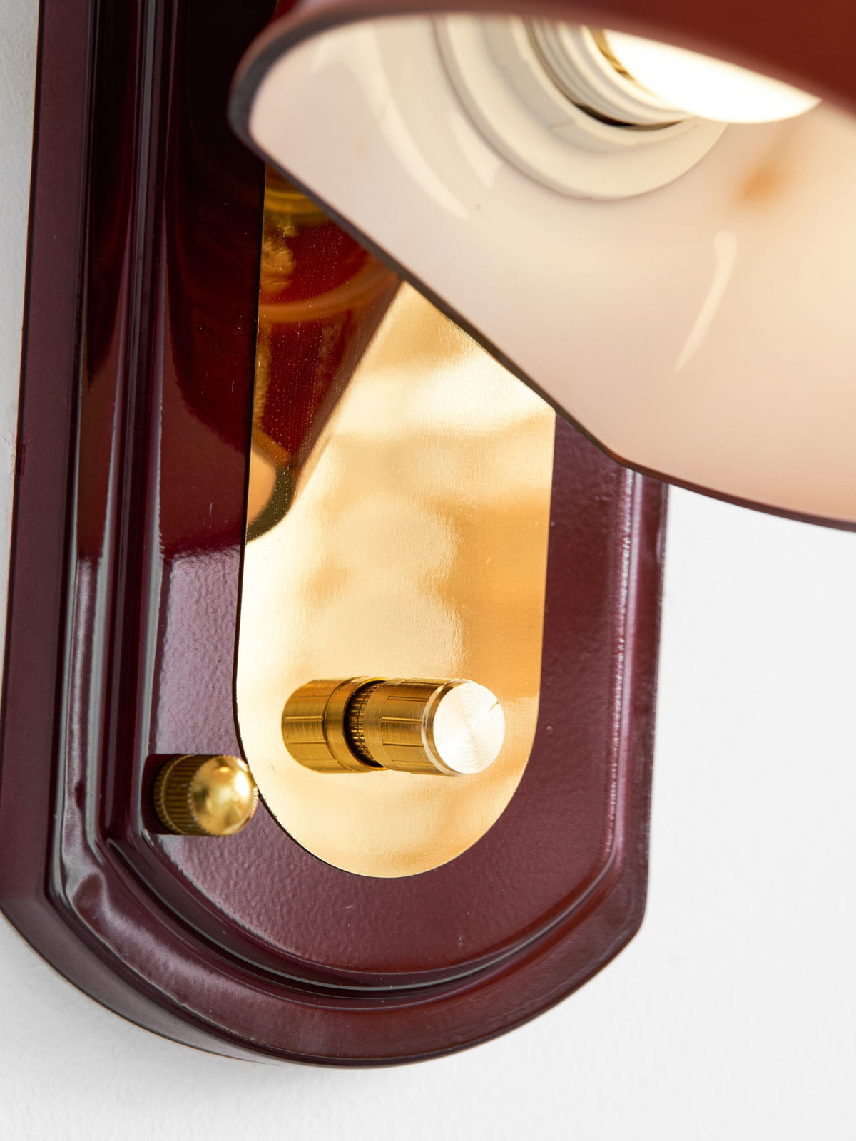 Close view of the red backplate, gold panel and brass knob on this Clérachic wall light, with the dome's inner socket above.