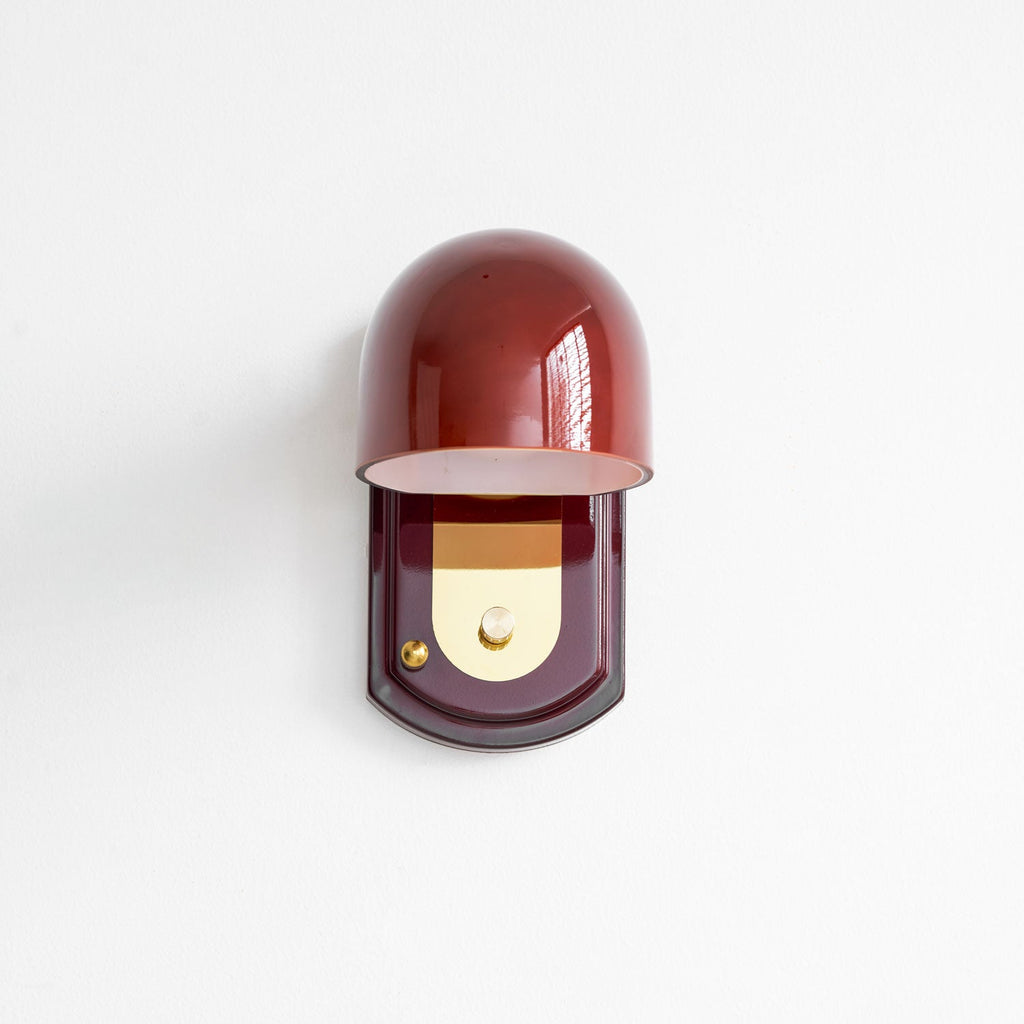 Front view of this Clérachic wall light on a white wall, the glossy red dome tilted over a gold panel on an oval red plate.