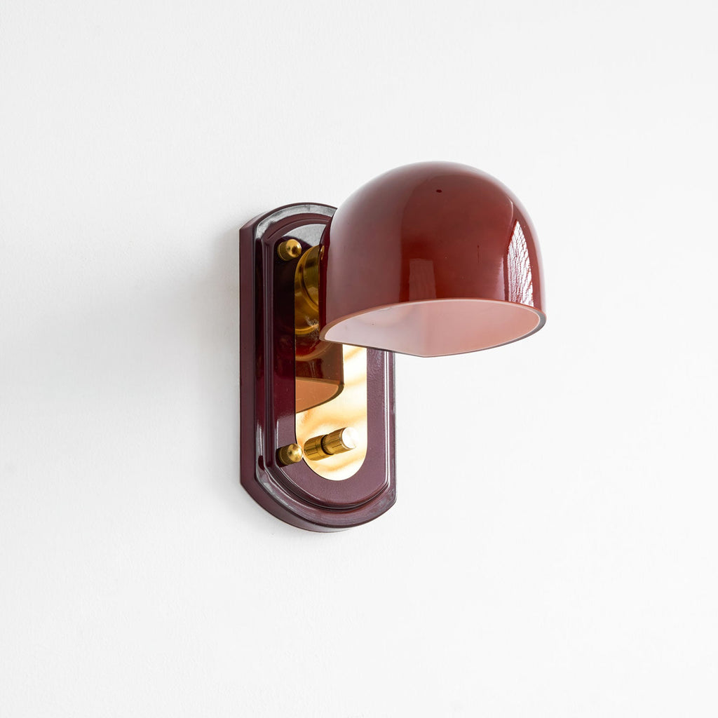 Three-quarter view of this Clérachic wall light on a white wall, with the glossy red dome angled out from the gold and red backplate.