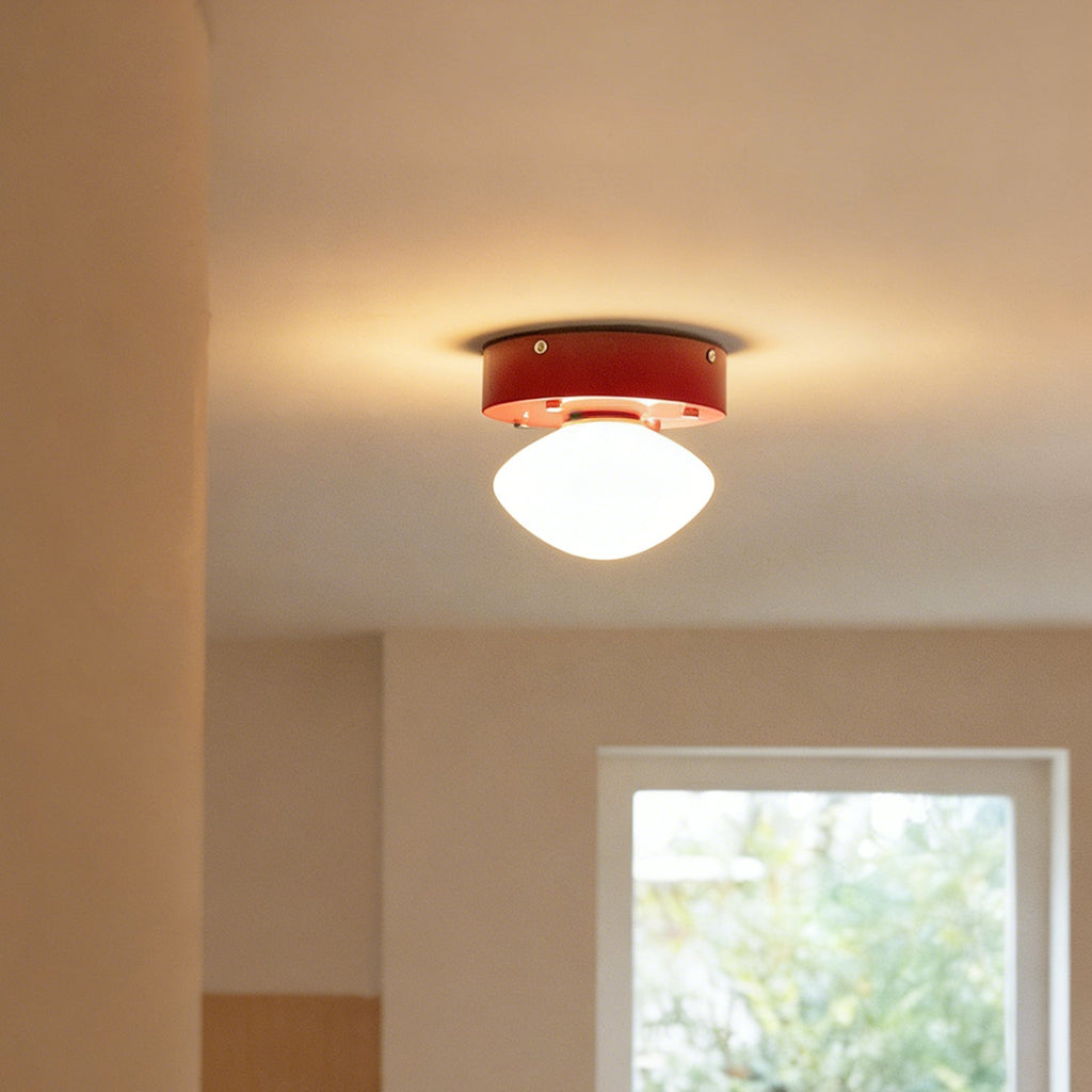 Distant view of a Clérachic flush mount glowing warm white on a ceiling, with a red canopy and a window in the room behind.