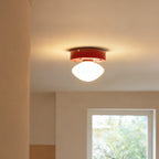 Distant view of a Clérachic flush mount glowing warm white on a ceiling, with a red canopy and a window in the room behind.