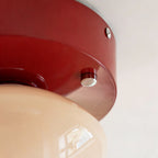 Close view of the red lacquered canopy and one silver stud on this Clérachic flush mount, with the beige glass dome below.