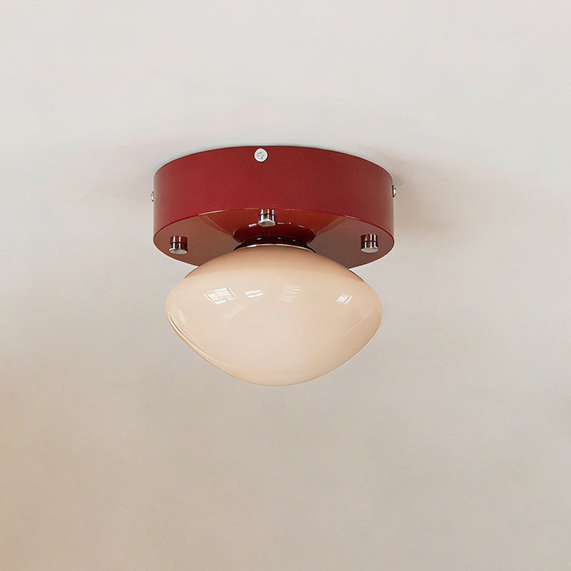 Front view of a Clérachic flush mount on a white ceiling, with a red round canopy and a rounded beige glass dome.