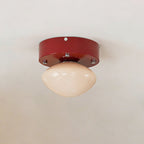 Front view of a Clérachic flush mount on a white ceiling, with a red round canopy and a rounded beige glass dome.