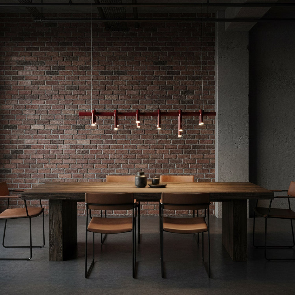 Linear red Clérachic chandelier with six arched heads, hung against dark brick above a rustic table and leather chairs.