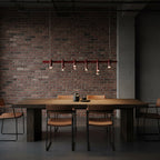 Linear red Clérachic chandelier with six arched heads, hung against dark brick above a rustic table and leather chairs.