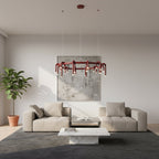 A red Clérachic ring chandelier above a cream sofa and a white marble coffee table, in a pale room with a large abstract artwork.