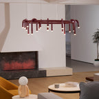 Red Clérachic ring chandelier seen at a slight angle in front of a white fireplace, with a plant and wooden floor beyond.