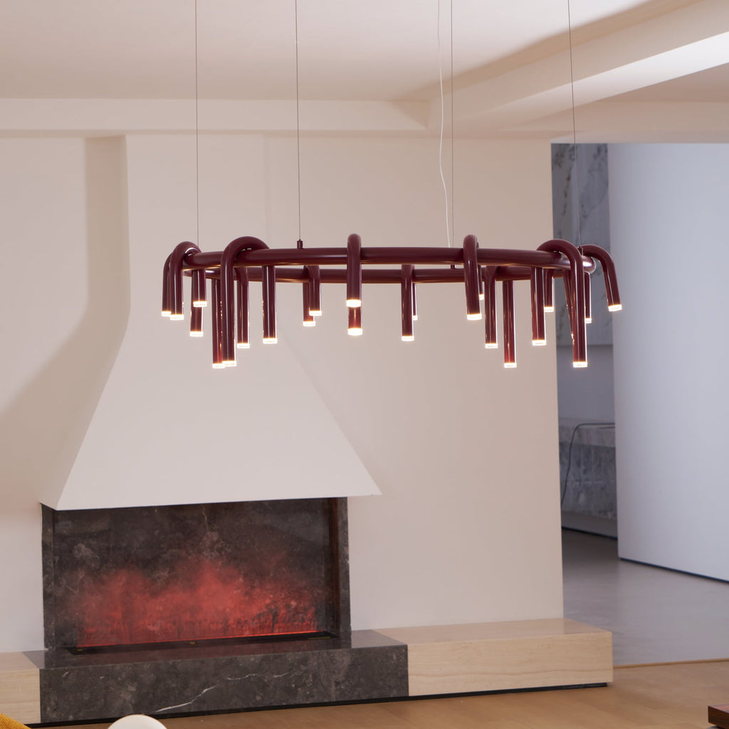 A red Clérachic ring chandelier above a low fireplace with a glowing ember-style panel, in a bright open room.