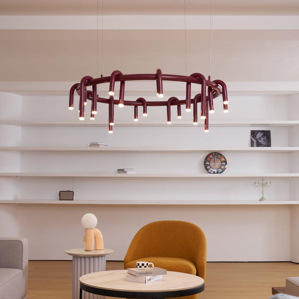 Red Clérachic ring chandelier in front of open white shelves, above an ochre armchair and a round marble table.