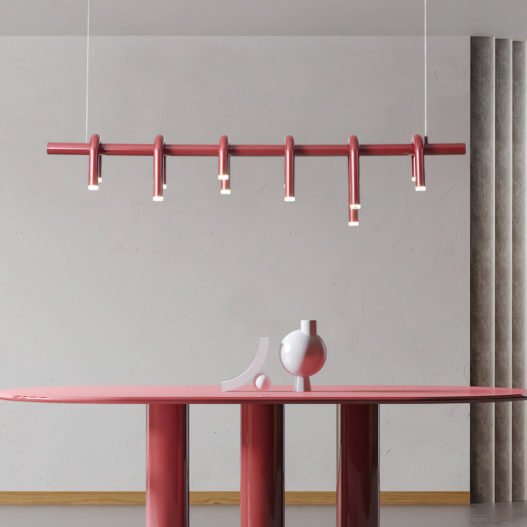 Close view of a red linear Clérachic chandelier, six slim arched heads along the bar, above a red oval table.