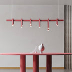Close view of a red linear Clérachic chandelier, six slim arched heads along the bar, above a red oval table.