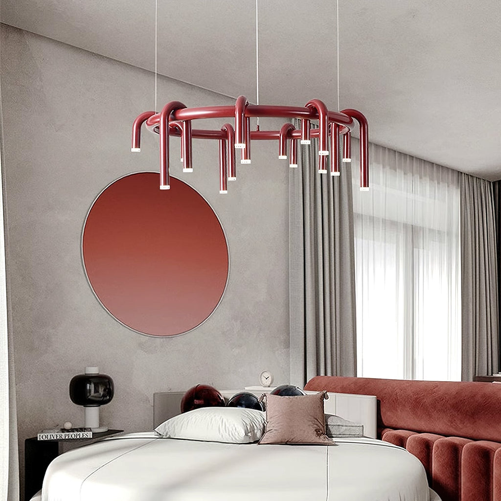 Red Clérachic ring chandelier above a bed with a burgundy velvet headboard, beside a round red mirror on a grey wall.