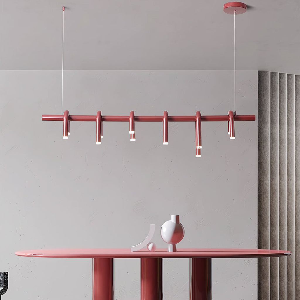 Linear red Clérachic chandelier with six short arched heads, hung above a red oval table with a sculptural vase.