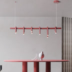 Linear red Clérachic chandelier with six short arched heads, hung above a red oval table with a sculptural vase.