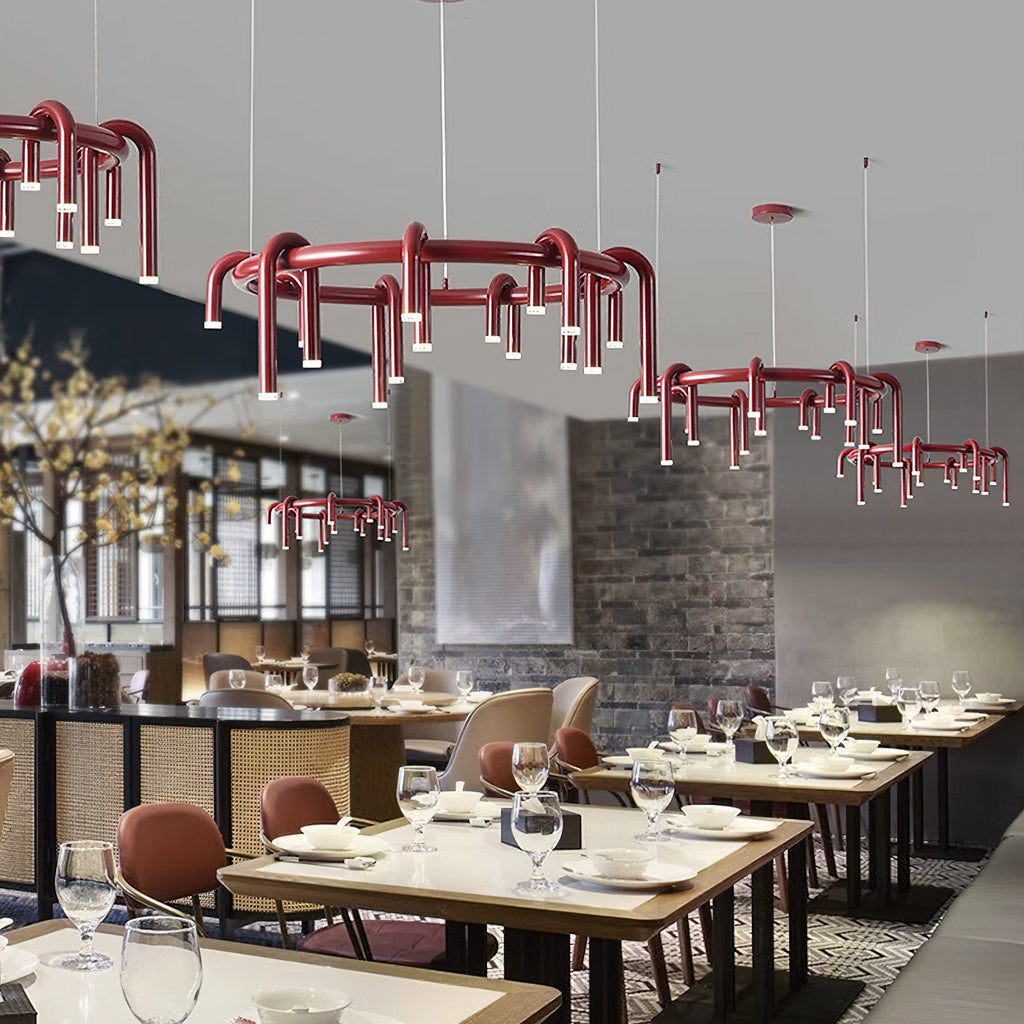 Red Clérachic chandeliers in several sizes hang in a restaurant, with set tables, glassware and a brick-and-timber wall behind.