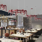 Red Clérachic chandeliers in several sizes hang in a restaurant, with set tables, glassware and a brick-and-timber wall behind.