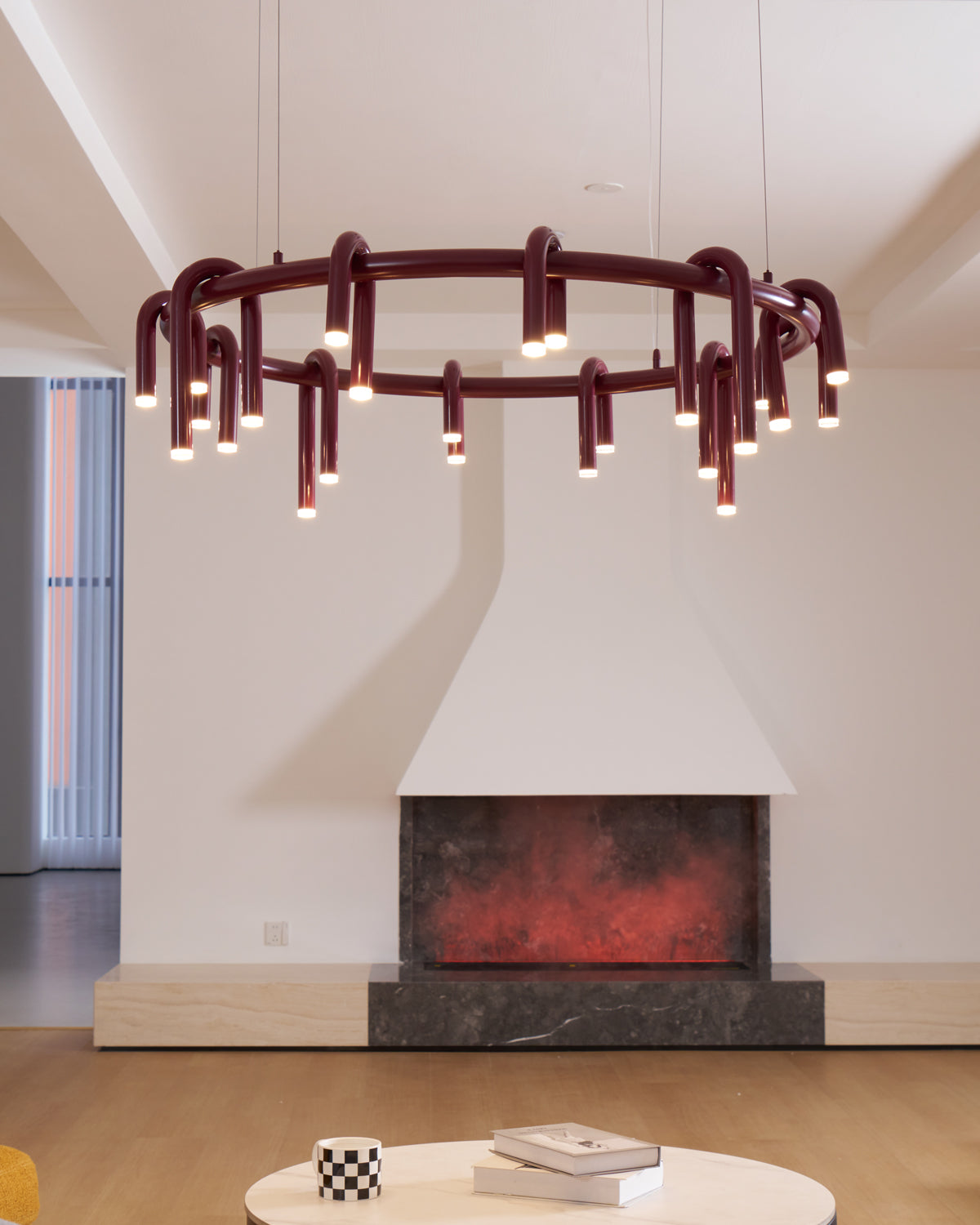Red Clérachic ring chandelier centred before a white fireplace, with an ember-style glow below and a coffee table in the foreground.